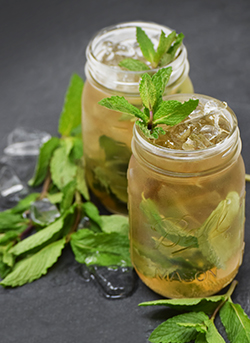 Mint julep cocktails in mason jars on a slate backdrop with mint garnish